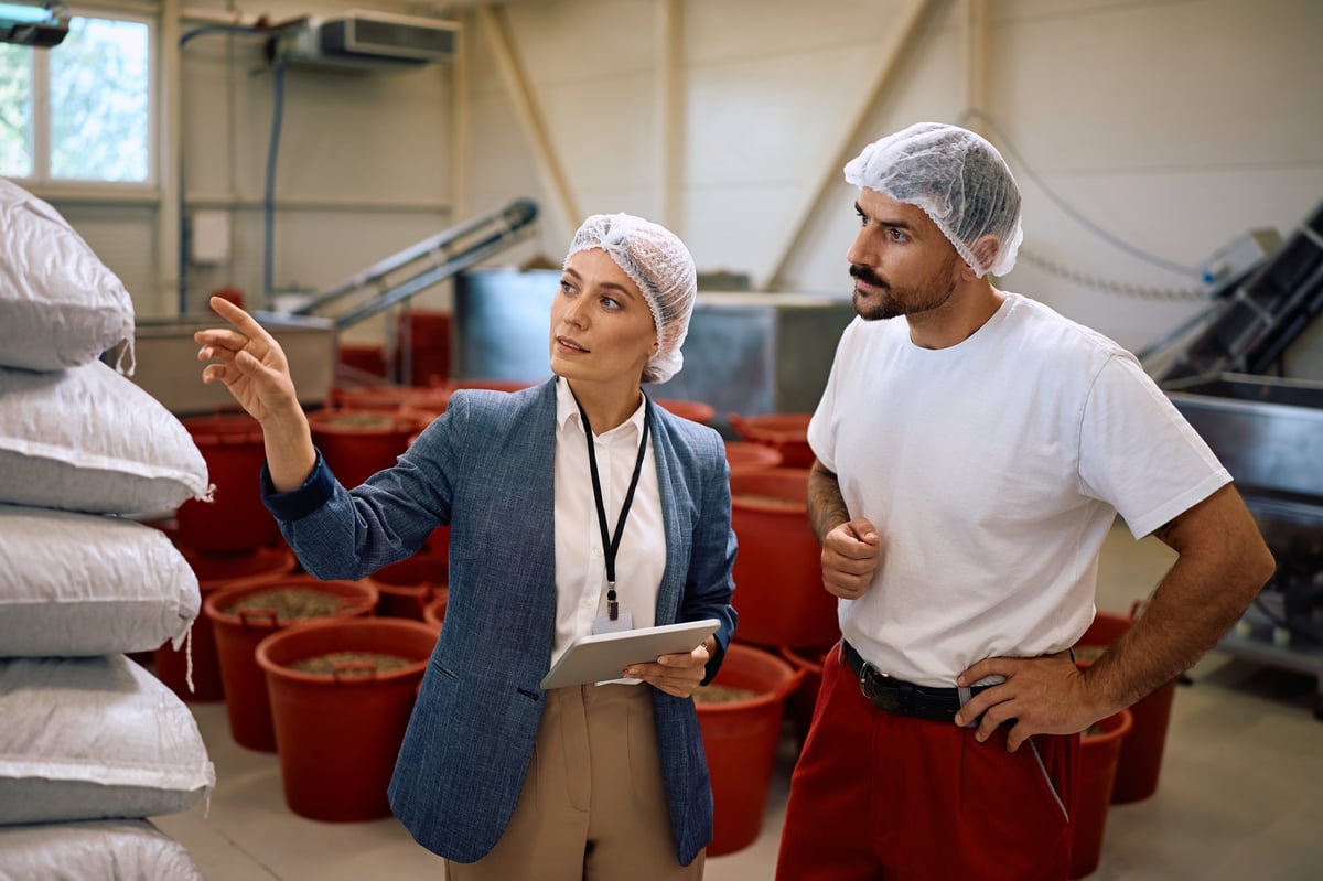 Quality control manager speaking with a worker while inspecting processed goods in a food factory