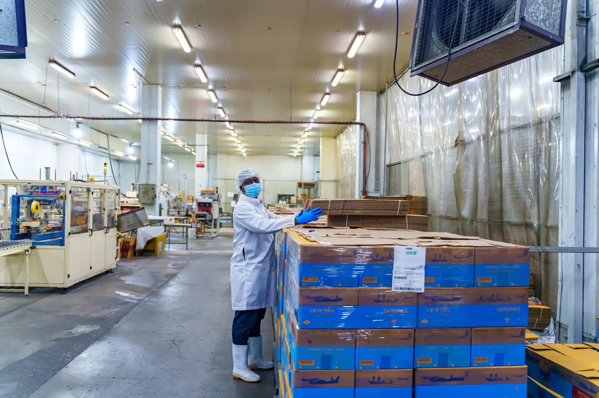 Worker in hairnet, mask, and gloves beside stacked finished cases in a clean industrial facility