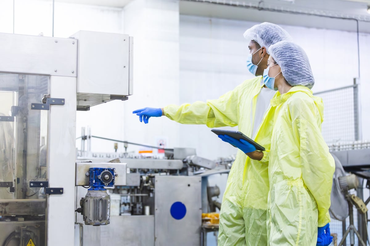 Quality control team in protective suits inspecting automated equipment on a food production line